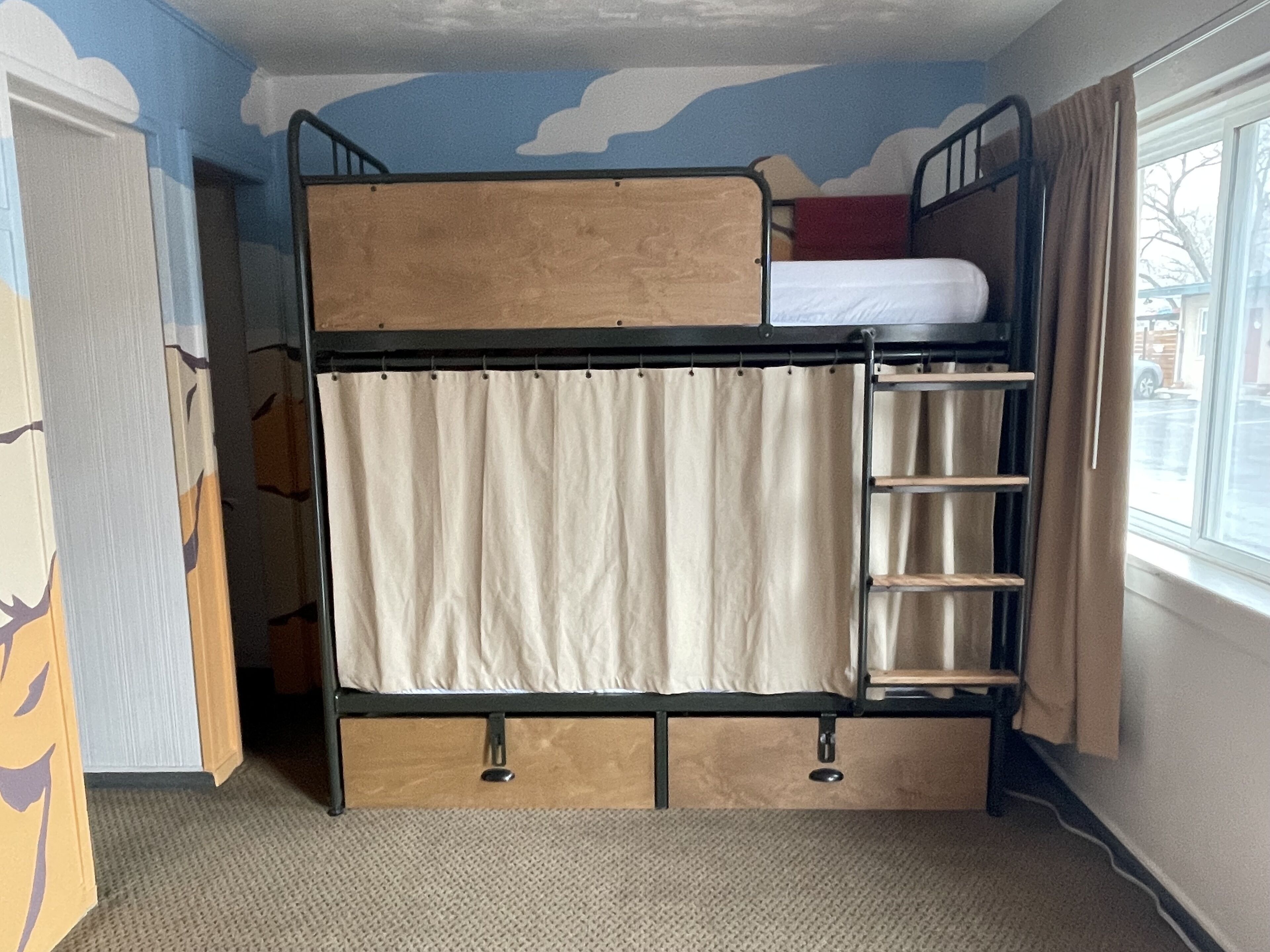 A bunk bed with a ladder, a window with curtains, and a door with a patterned design.