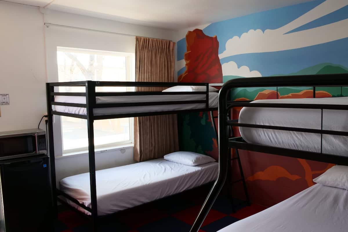 Un dormitorio con literas, una ventana con cortinas, un microondas y un mural en la pared.