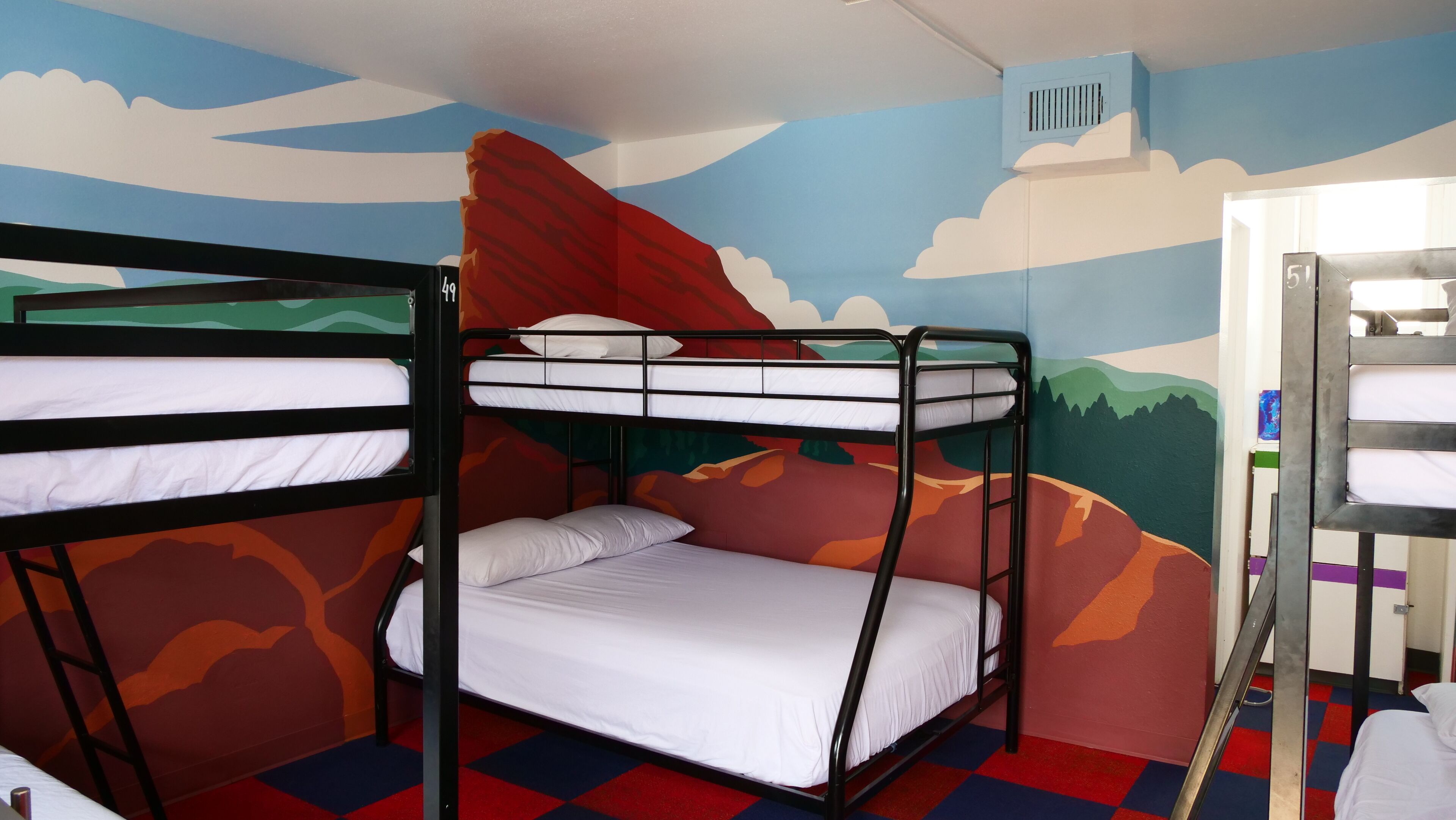 A bunk bed room with a mural of a landscape, a window, and a door.
