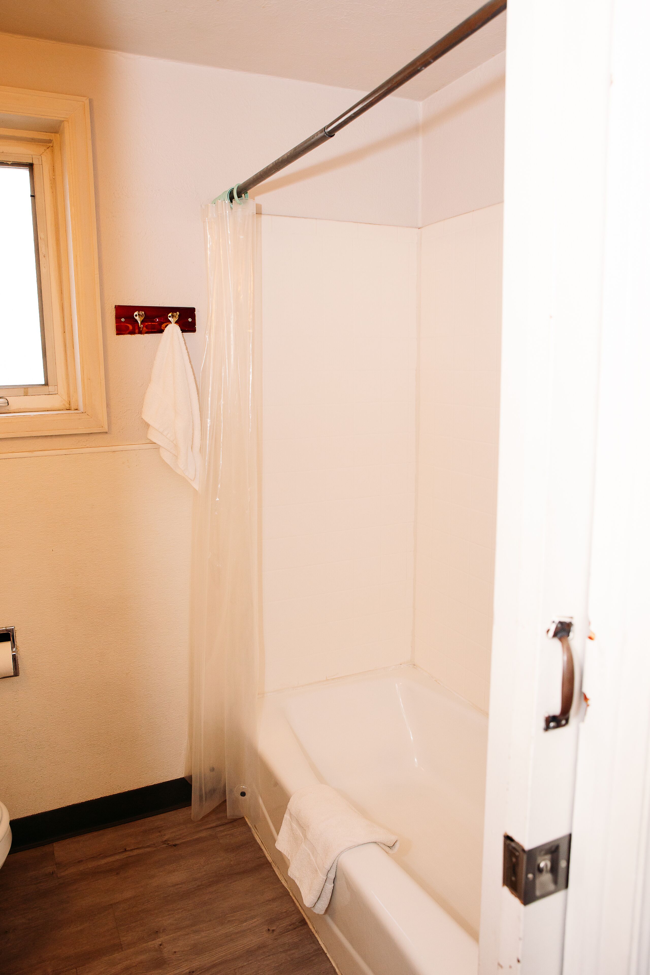 A bathroom with a bathtub, a shower curtain, a towel rack, and a wooden floor.