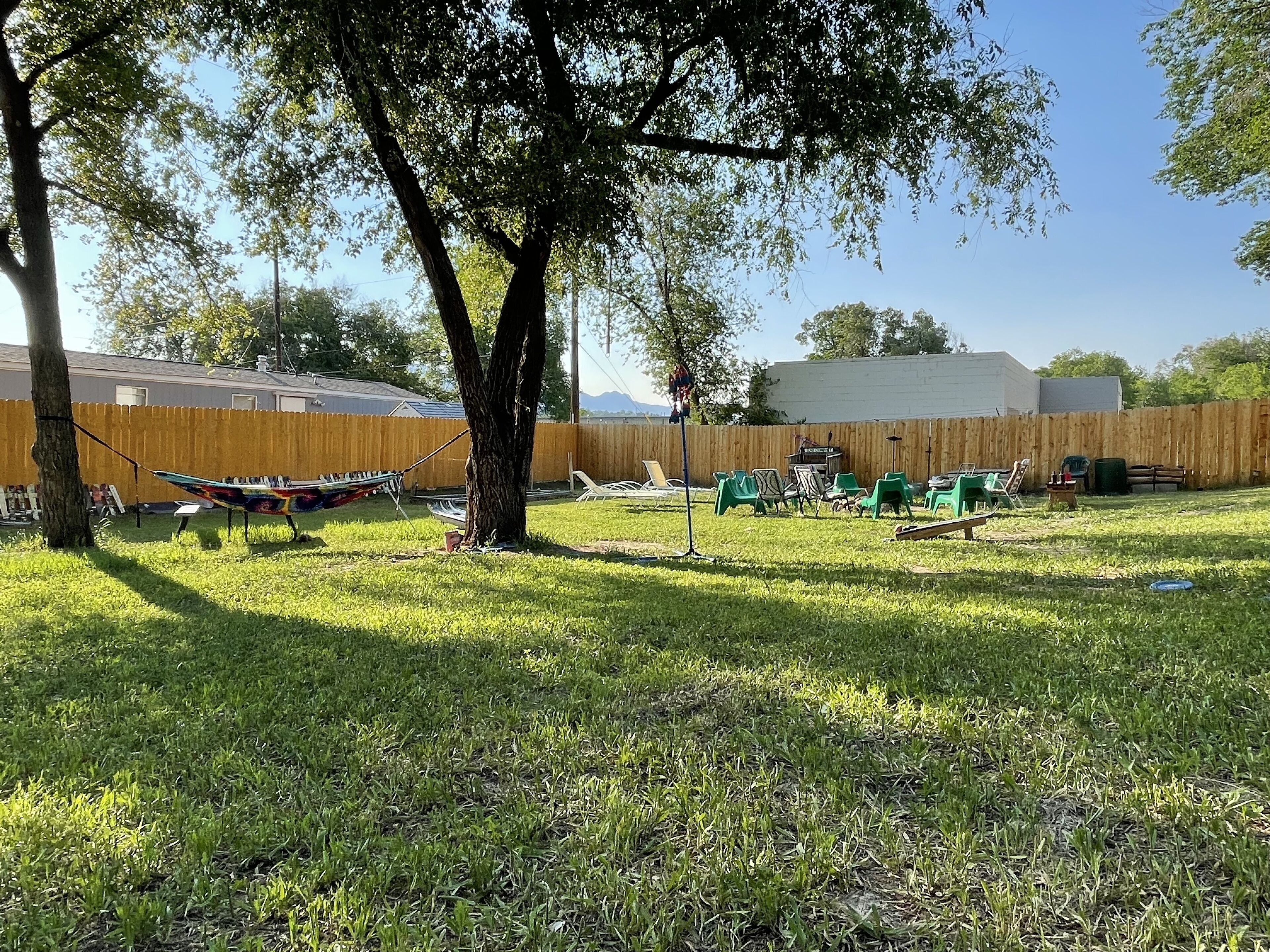 A backyard with a hammock, lawn chairs, and a wooden fence.