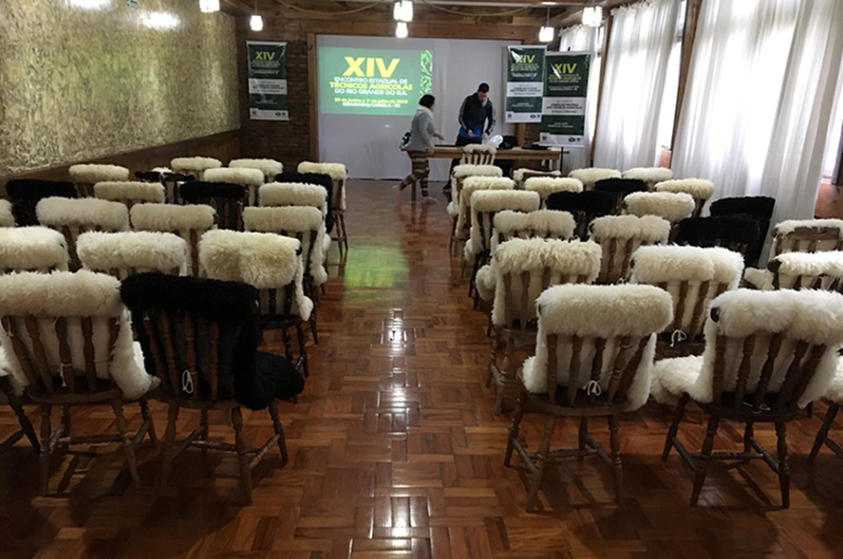 A conference room with rows of chairs, a wooden floor, and a presentation screen.