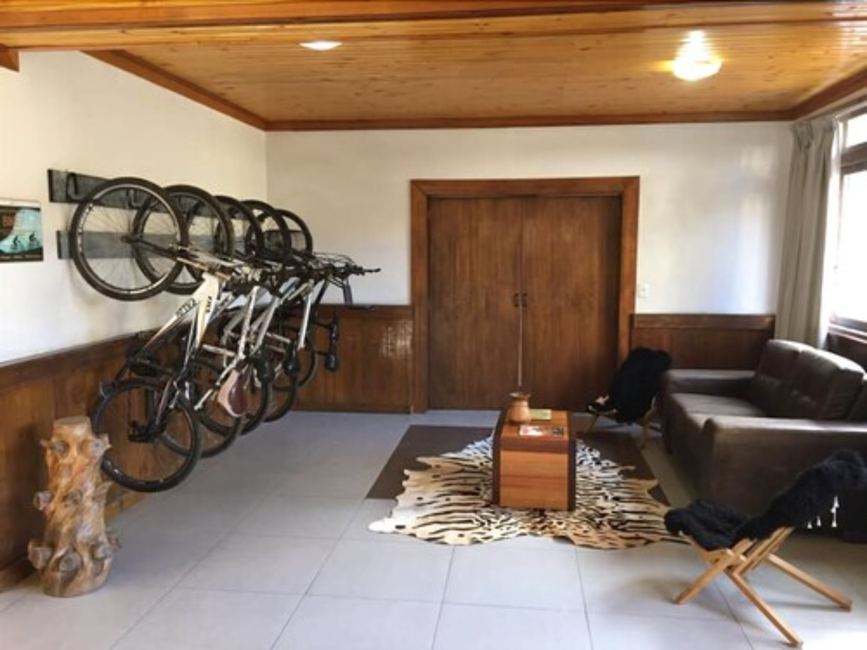 A room with a wooden ceiling, a mounted bicycle rack, a wooden door, a brown leather sofa, a wooden coffee table, and a zebra print rug.