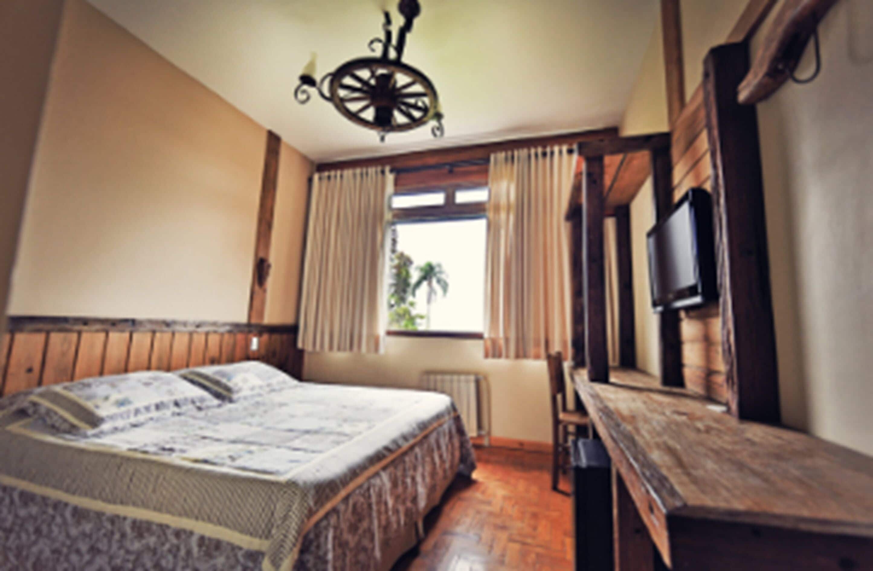 A bedroom with a large bed, wooden furniture, a window with curtains, and a television on the wall.