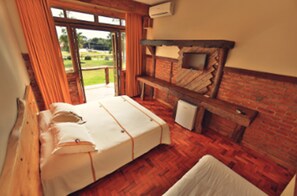 A room with a bed, a bench, and a small table. There is a window with curtains and a view of greenery outside. - Hotel Fazenda Pampas (Canela)