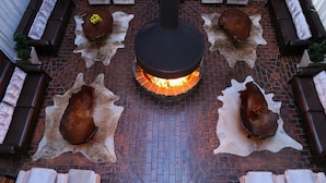 A central fire feature surrounded by seating areas with leather sofas and chairs, set on a brick floor. - Hotel Fazenda Pampas (Canela)