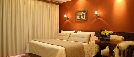 Una habitación de hotel con una cama grande, dos lámparas de pared, un cuadro, una mesita con flores y una silla.