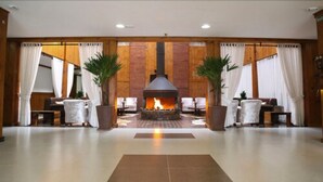A spacious lobby with a central fireplace, wooden paneling, and comfortable seating areas. - Hotel Fazenda Pampas (Canela)