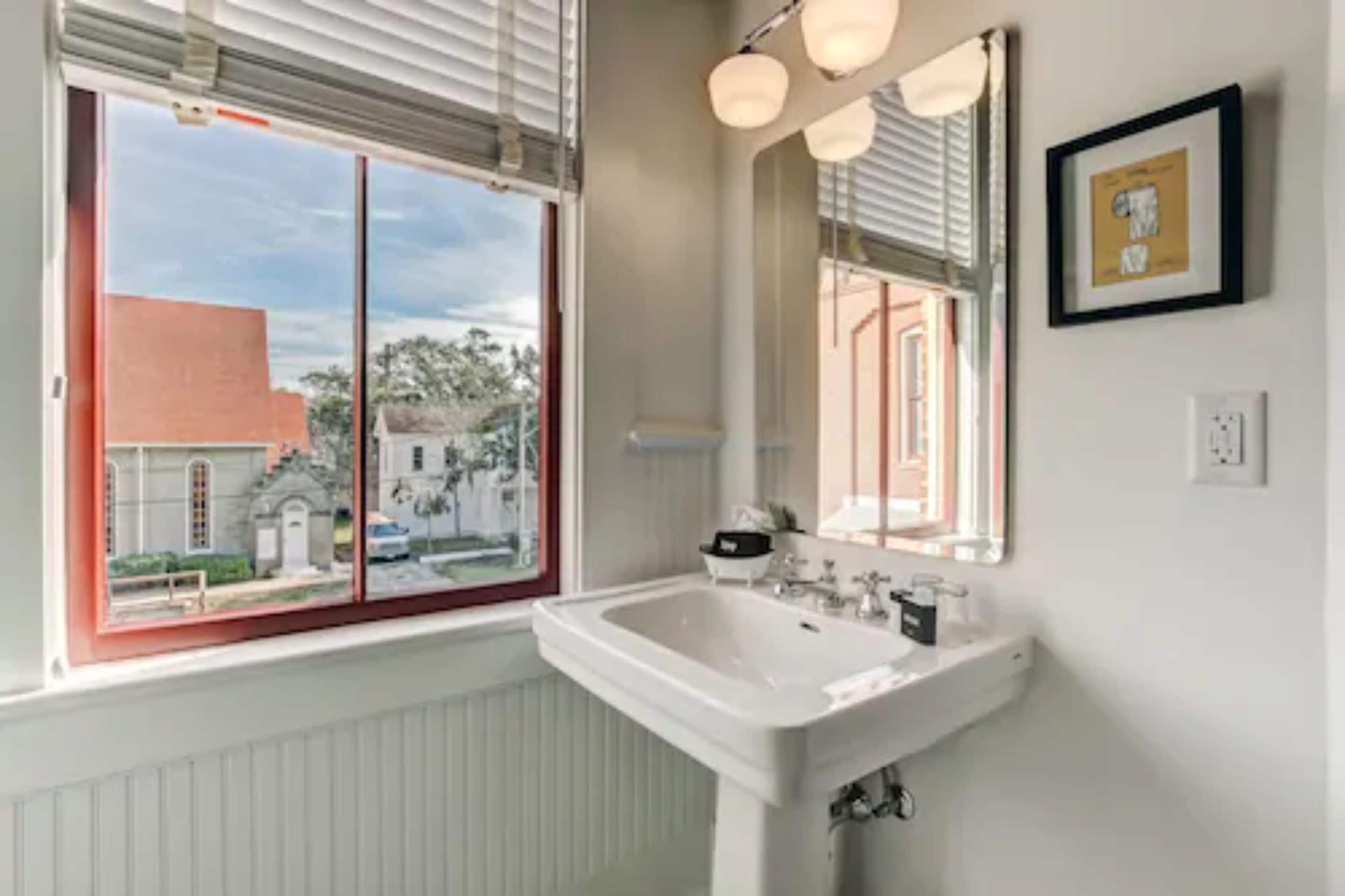 A bathroom with a white sink, a large mirror, and a window with blinds.
