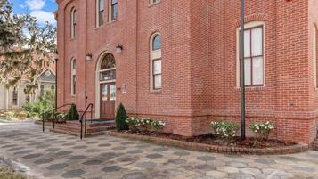 A red brick building with a central entrance, a covered porch, and a paved walkway.
