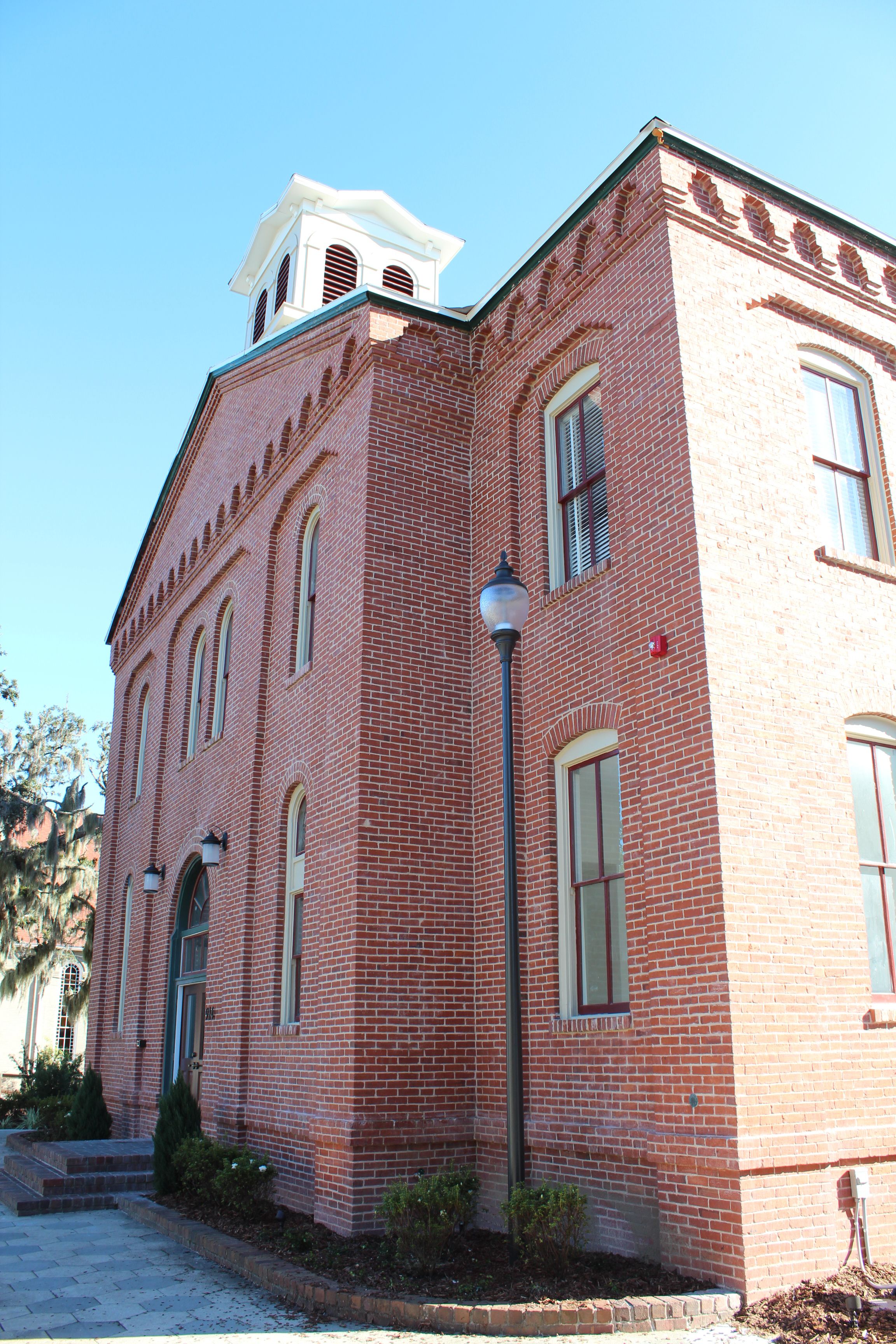 Un edificio de ladrillo rojo con una torre de campanas, ventanas arqueadas y un farol.