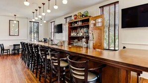 A bar area with wooden bar counter and chairs, a shelf with bottles, and a TV mounted on the wall. - Amelia Schoolhouse Inn (Fernandina Beach)