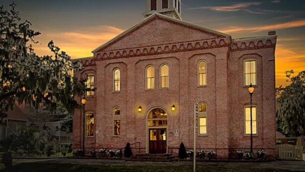 A brick building with a central entrance, arched windows, and a bell tower. - Amelia Schoolhouse Inn (Fernandina Beach)