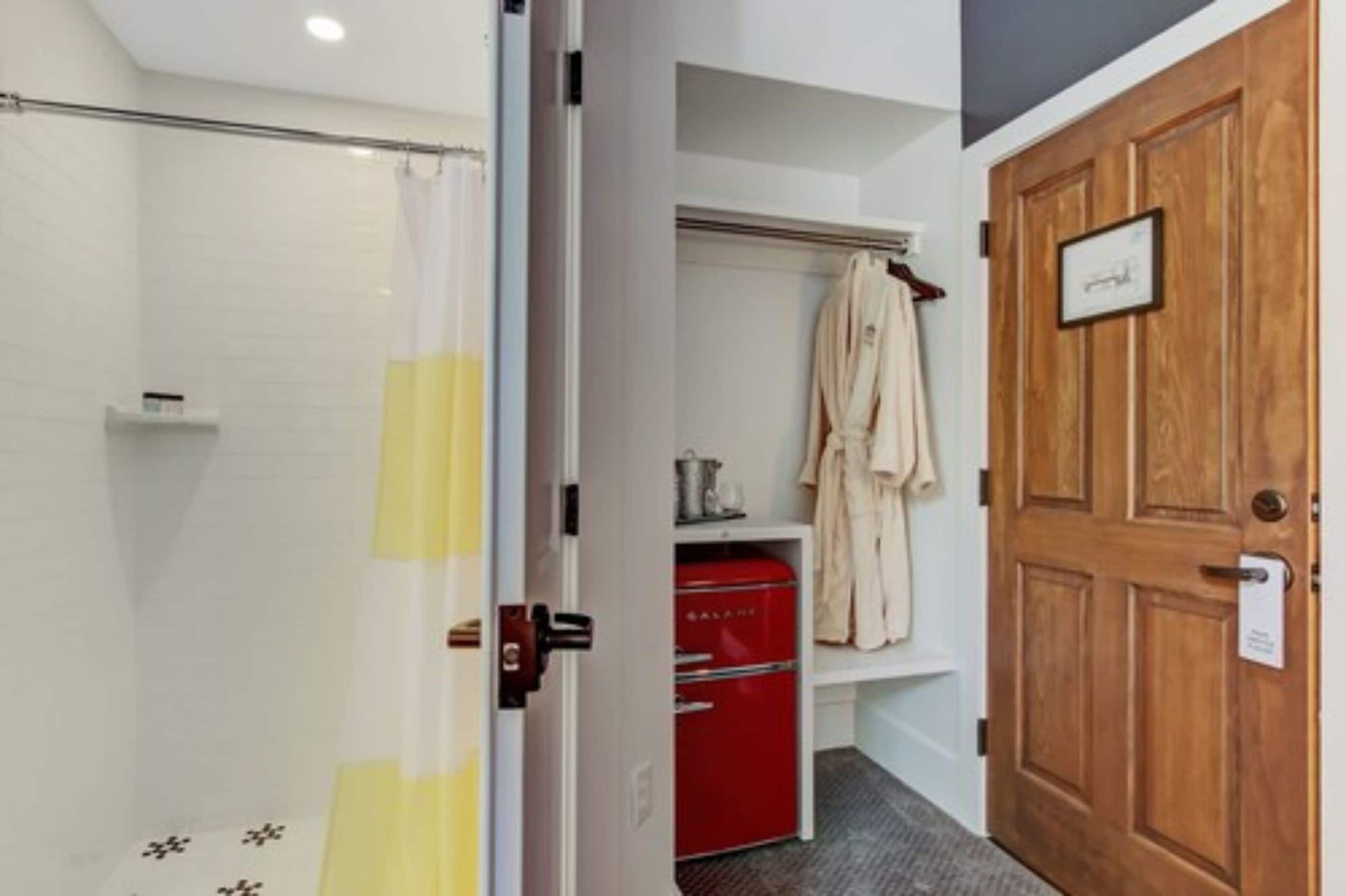 Un baño con ducha, un almacenaje rojo, una puerta de madera y una bata colgada en un perchero.