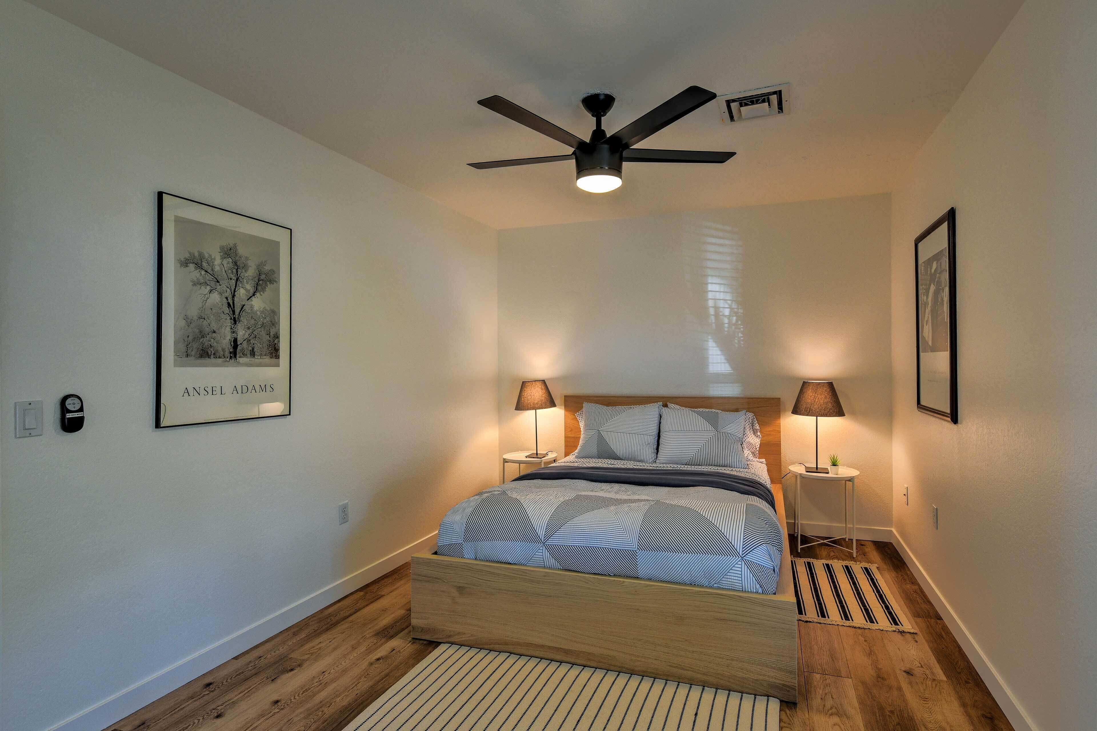 A bedroom with a bed, two bedside lamps, a ceiling fan, and a framed picture on the wall.