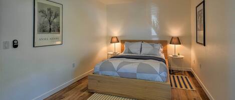 A bedroom with a bed, two bedside lamps, a ceiling fan, and a framed picture on the wall.
