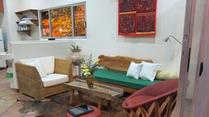 A cozy living room with a wicker sofa, a wooden coffee table, and a red cushioned stool.