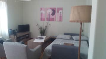 A compact living room with a sofa, a small table, a TV, and a lamp.