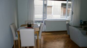 A dining area with a table, chairs, a radiator, and a window with curtains.