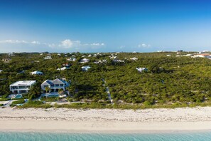 An aerial view of a coastal area with multiple houses surrounded by dense vegetation and a beach.