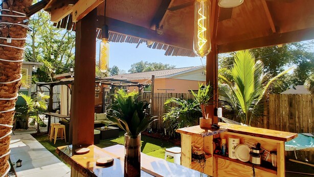 A wooden outdoor bar area with a clear view of the backyard, including a wooden fence, palm trees, and a small pool. - With Oasis Shared Backyard (St. Petersburg)