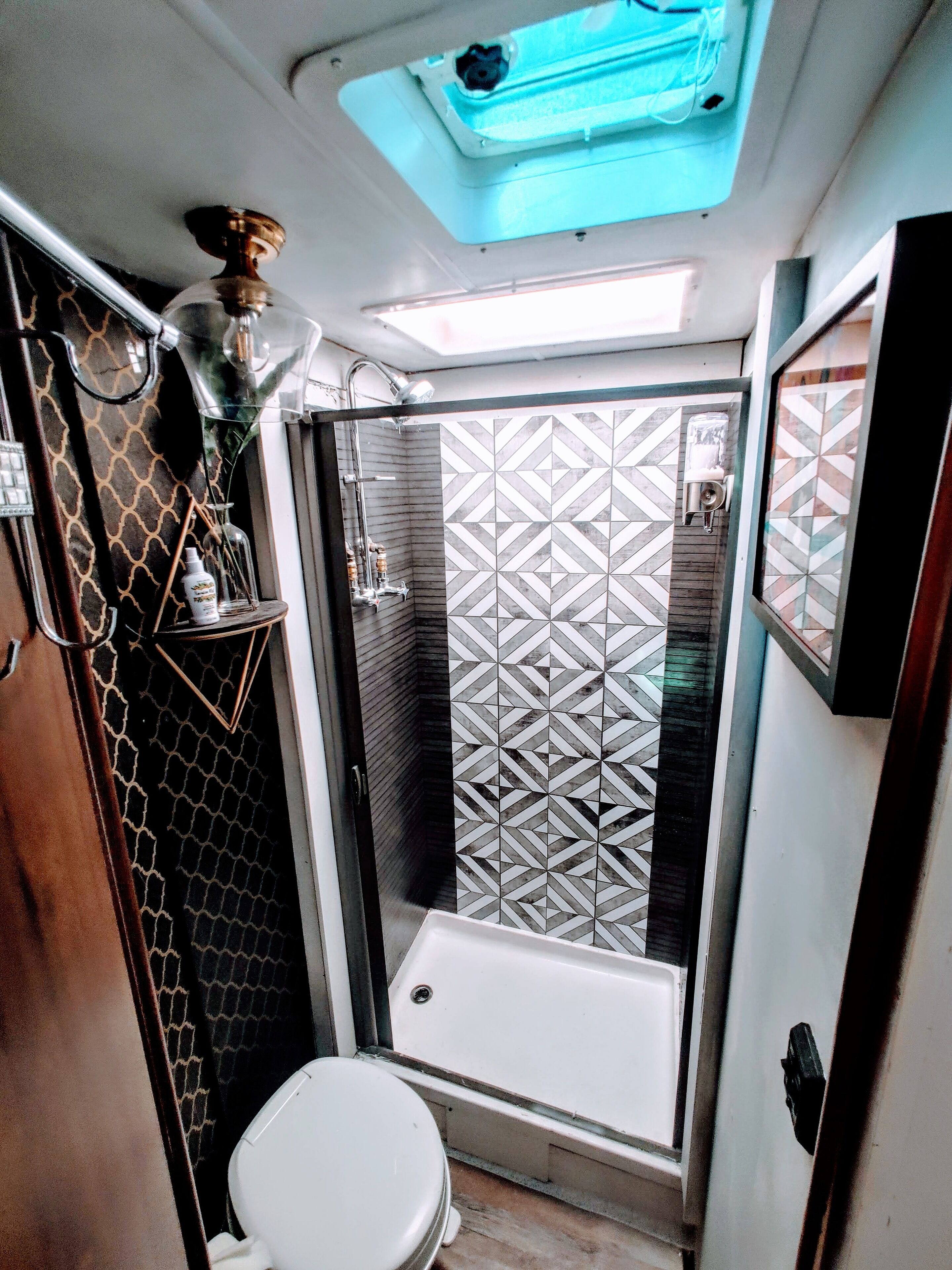 A compact bathroom with a shower, toilet, and a small shelf with toiletries.