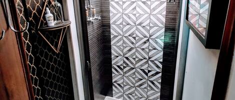 A compact bathroom with a shower, toilet, and a small shelf with toiletries.