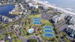 Eine Vogelperspektive auf einen Küstenkurort mit mehreren Gebäuden, einem Strand und einem Tennisplatzkomplex.