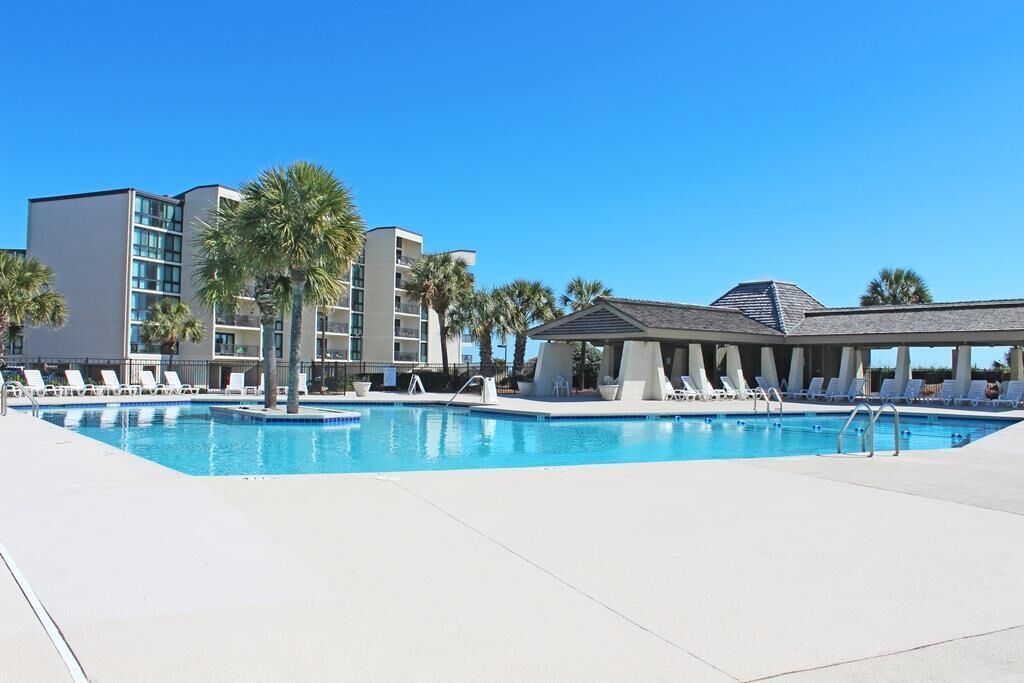 A swimming pool with lounge chairs, palm trees, and modern buildings in the background.