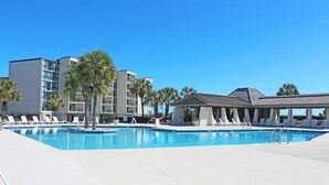 Ein Schwimmbecken mit Liegestühlen, Palmen und modernen Gebäuden im Hintergrund.