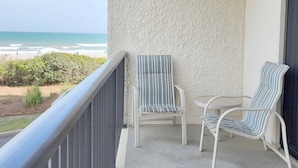 Ein Balkon mit zwei gestreiften Stühlen, einem kleinen runden Tisch und Blick auf den Strand.