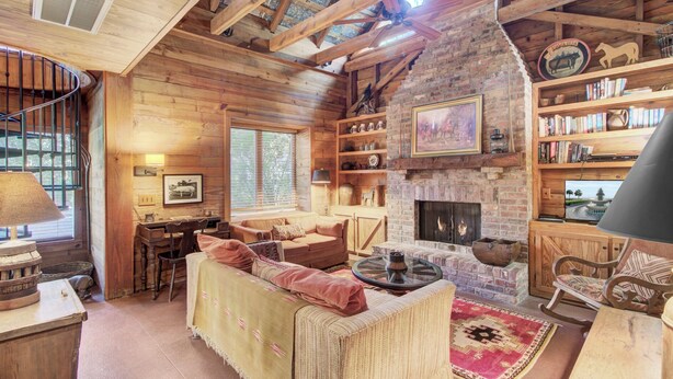 Interior rústico de una cabaña con chimenea, paredes de madera, zona de comedor y una estantería.
