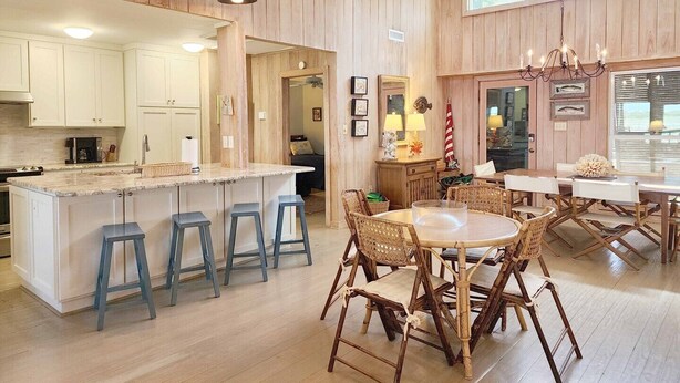 A spacious kitchen with wooden paneling, a central island with stools, and a dining area with wicker chairs.