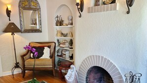 Una sala de estar acogedora con chimenea, una mesa de centro de vidrio, un tapete estampado y una estantería con adornos.