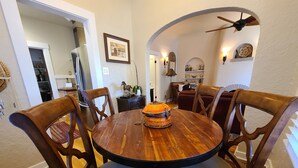 Un comedor con una mesa redonda de madera rodeada de cuatro sillas, un cuenco decorativo sobre la mesa y un ventilador de techo.