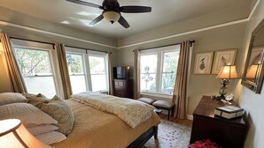 Un dormitorio con cama, ventilador de techo, cómoda, mesita de noche, lámpara y ventana con cortinas.