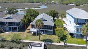 A coastal property with multiple buildings, including a large house with a balcony and a smaller structure with a covered porch. - Idyll Daze Beach Cottage on Saltwater Canal with Crab Dock (Pawleys Island)