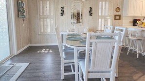 A dining area with a round table, white wicker chairs, and a chandelier. - Idyll Daze Beach Cottage on Saltwater Canal with Crab Dock (Pawleys Island)