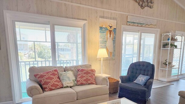 A cozy living room with a beige sofa, a blue armchair, and a glass coffee table. - Idyll Daze Beach Cottage on Saltwater Canal with Crab Dock (Pawleys Island)