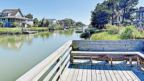 A wooden dock extending into a calm river, surrounded by houses with a clear sky above. - Idyll Daze Beach Cottage on Saltwater Canal with Crab Dock (Pawleys Island)