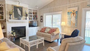 A living room with a fireplace, a sofa, a coffee table, and a bookshelf. - Idyll Daze Beach Cottage on Saltwater Canal with Crab Dock (Pawleys Island)