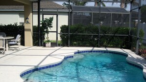 A swimming pool with a curved edge and blue tiles, surrounded by a covered patio area with chairs and a table.