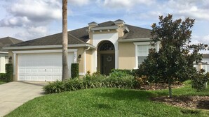 A single-story house with a garage, a front door, and a small tree in the front yard.