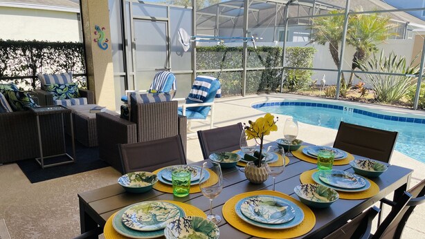 An outdoor dining area with a pool, wicker furniture, and tropical decor.