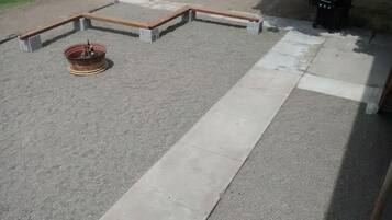 Un chemin en béton mène à un espace agrémenté de bancs en bois et doté d’un foyer.