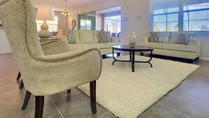 Una sala de estar con un sofá color beige, un sillón a juego, una mesa de centro y un ventanal con persianas.