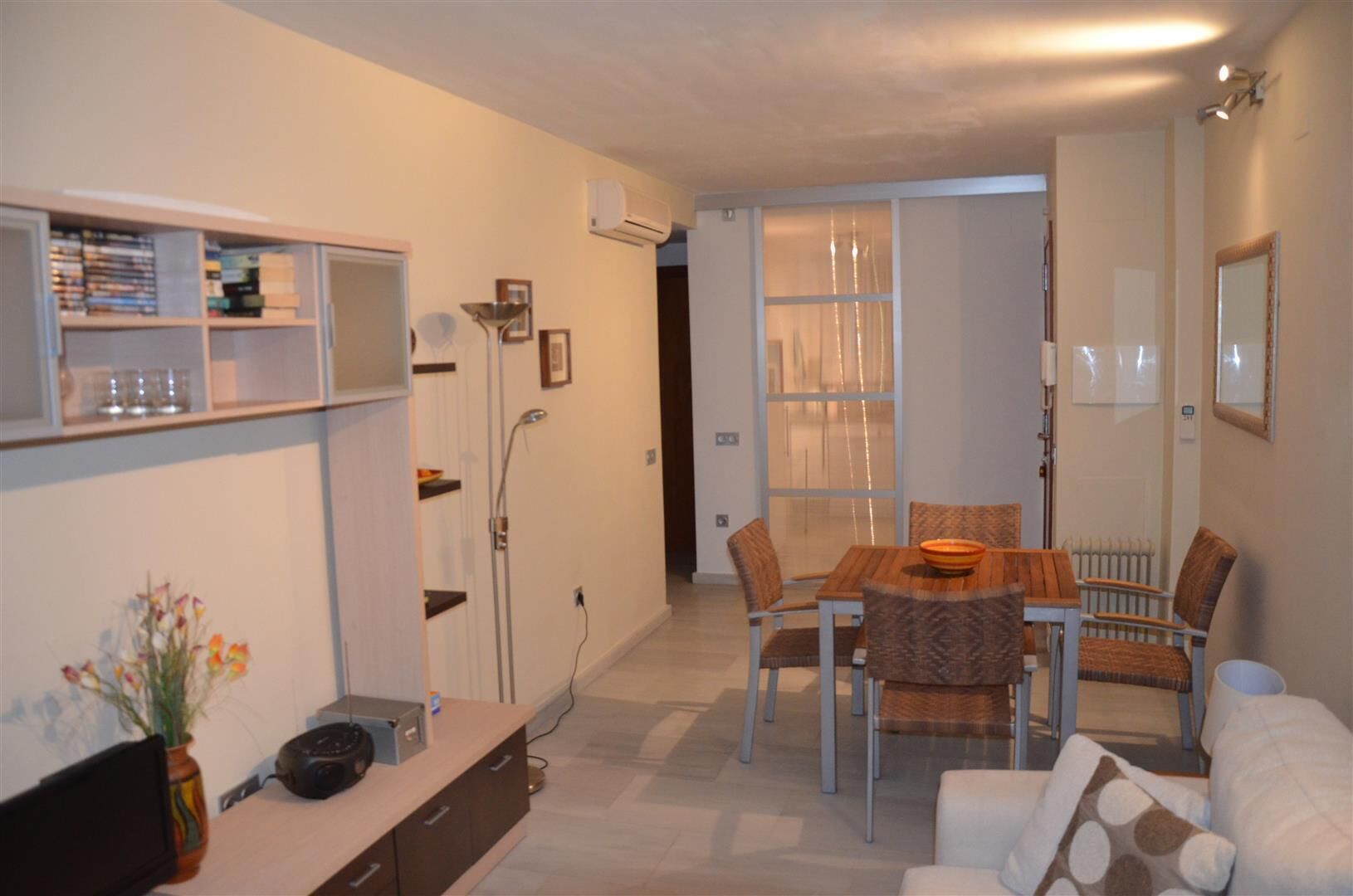 A modern living room with a dining area, featuring a sofa, a table with chairs, a bookshelf, and a radiator.