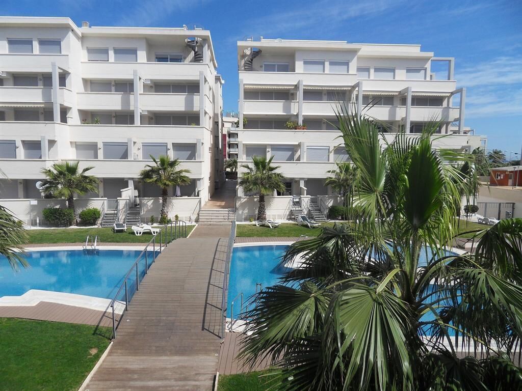 Un immeuble d’appartements moderne doté d’une piscine centrale, entouré de palmiers et agrémenté d’une terrasse en bois.