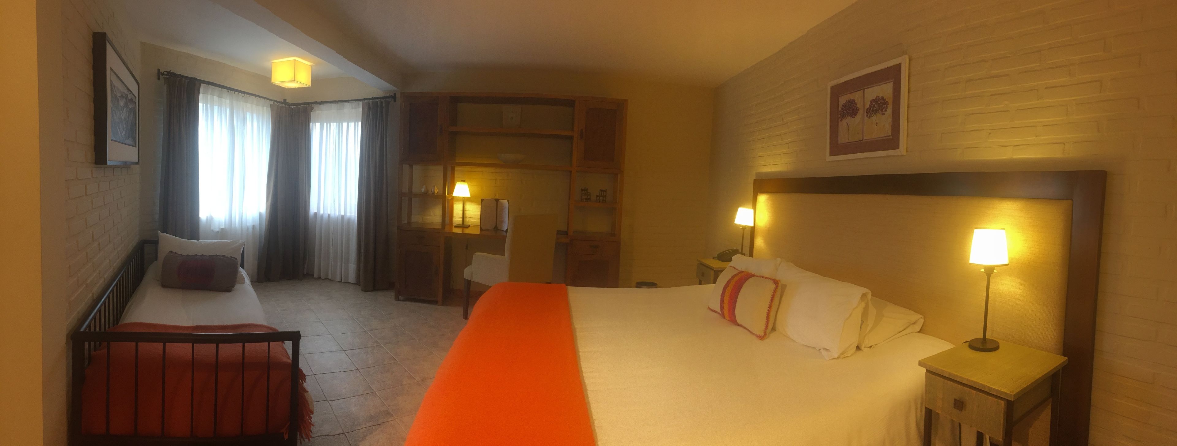 Habitación de hotel con cama, escritorio, silla, armario y mesita de noche con lámpara.