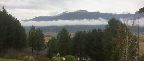 Vista de un paisaje montañoso con una casa en primer plano y una zona boscosa.
